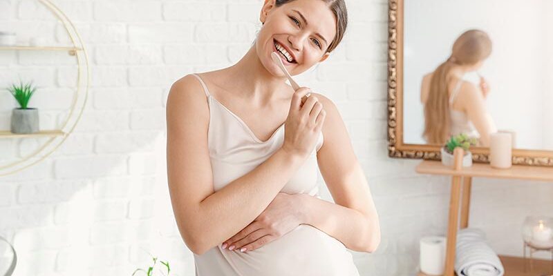 Young pregnant woman brushing teeth in bathroom